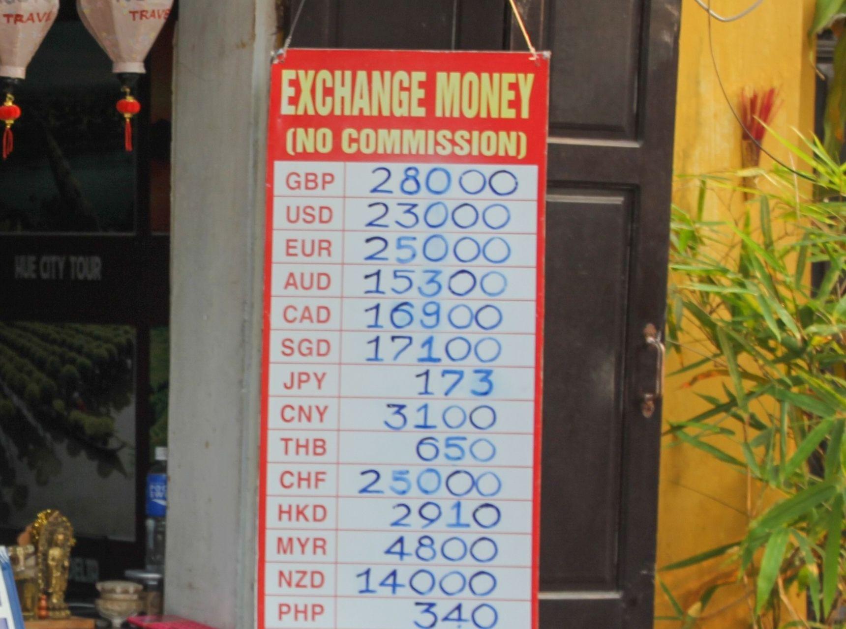 A handwritten exchange rate board hanging outside a shopfront in Vietnam, listing rates for pounds, dollars, euros and other currencies against the dong